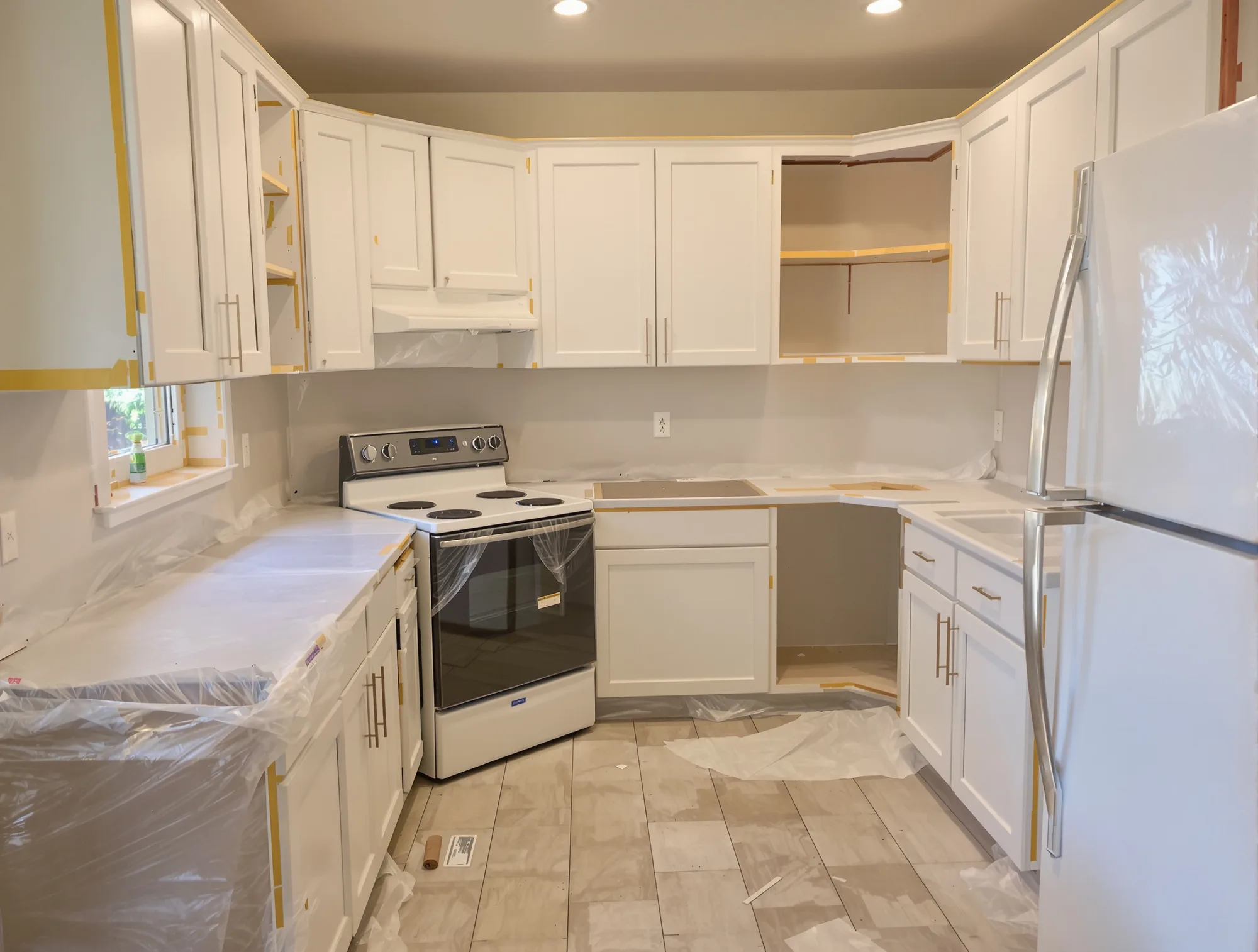 Kitchen with counters, appliances and floor covered in plastic and paper, cabinet doors removed