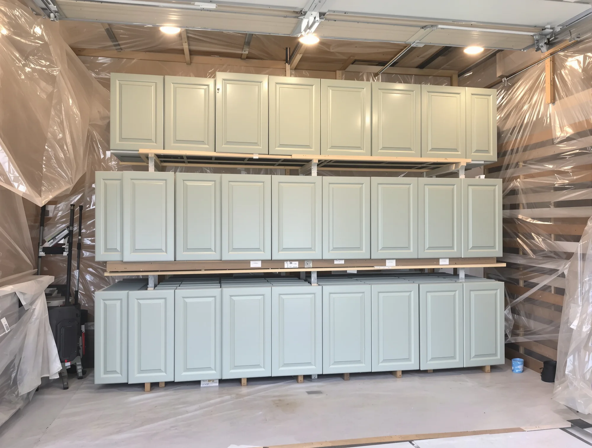 Rows of sprayed cabinet doors drying on tiered racks under bright work lights