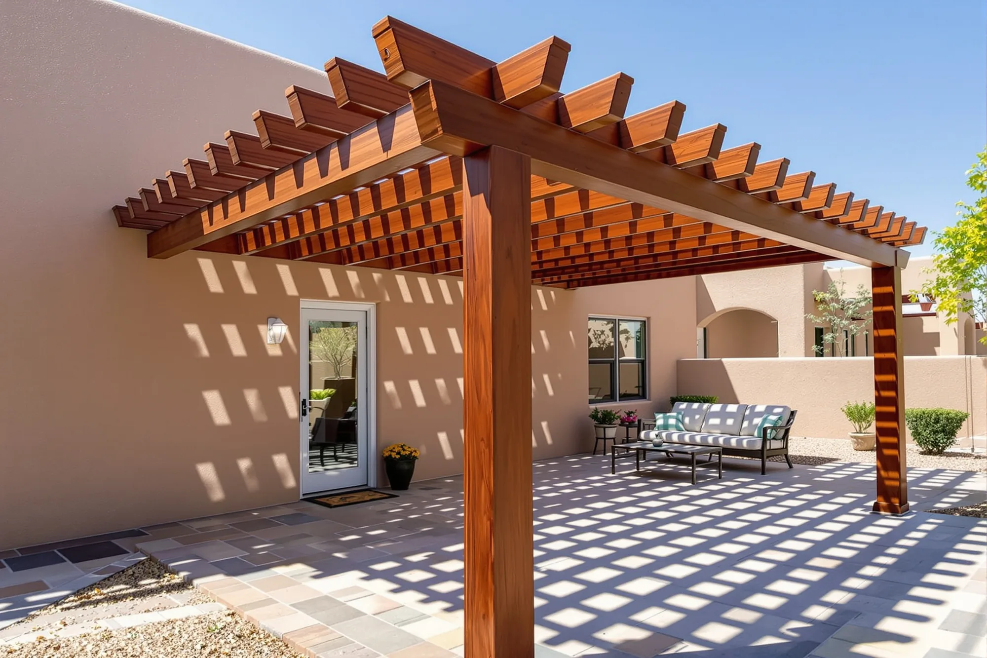 Freshly stained wood pergola over a flagstone patio beside a Pueblo Revival stucco home