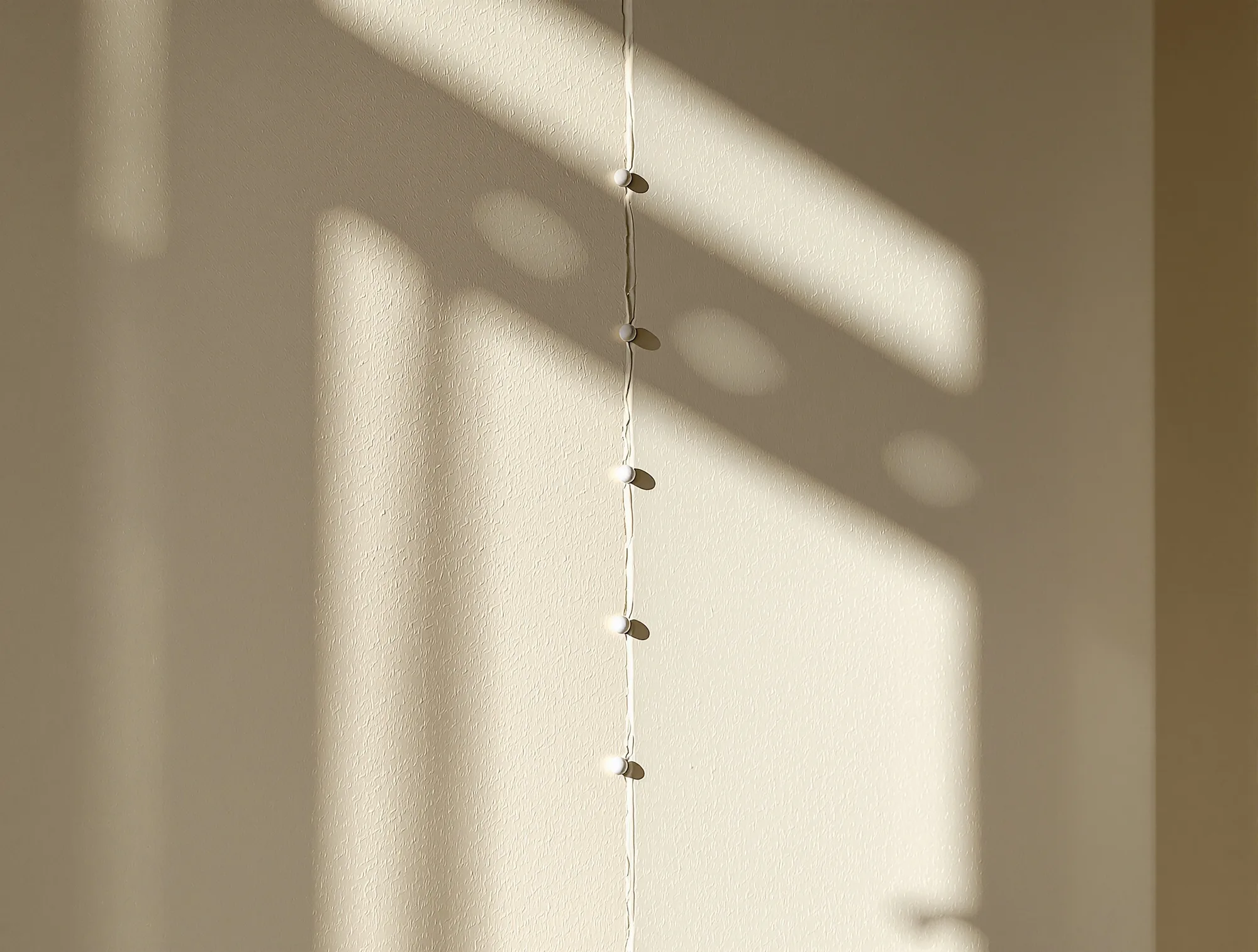 Row of small nail pops pushing through the paint on an off-white drywall wall in side light