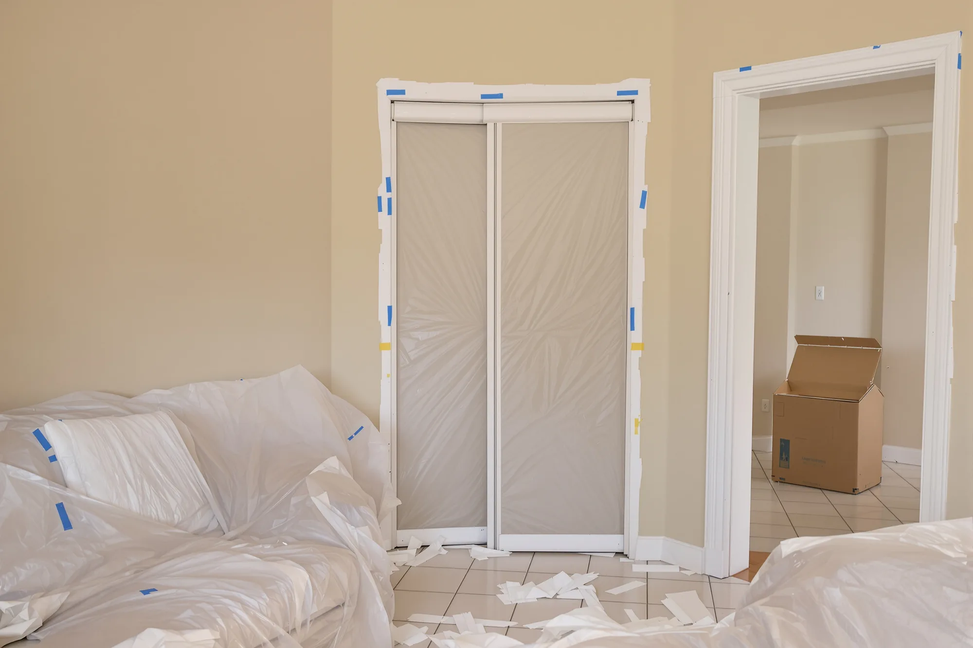 Room prepared for repairs with plastic over the furniture and a plastic dust door in the doorway