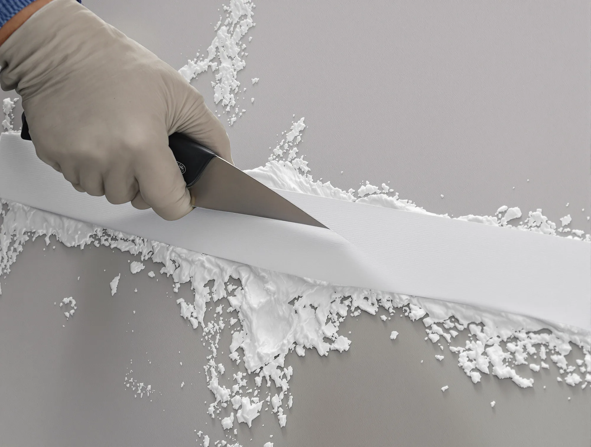 Paper tape bedded in joint compound along a patch seam with a taping knife pressing it flat