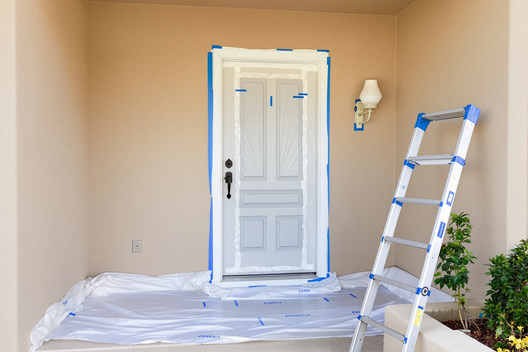 Front entry covered with drop cloths, the door hardware and porch light wrapped in plastic