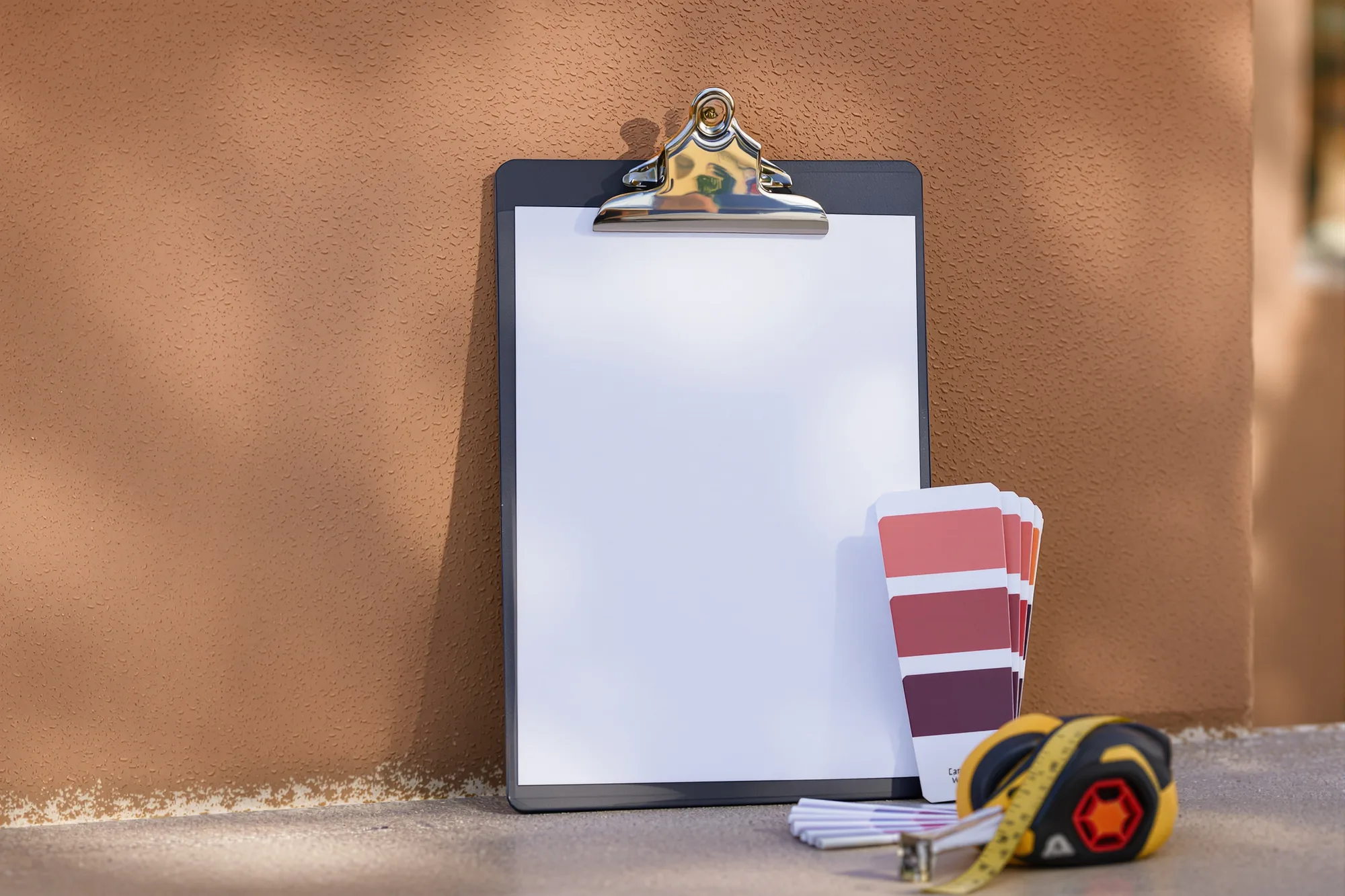 Clipboard, tape measure and a fan deck of color chips on a stucco garden wall