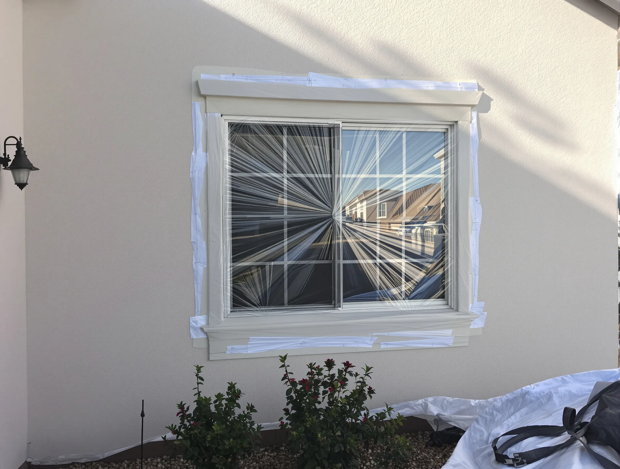 Stucco home window and trim masked with plastic and tape, drop cloths over the plants below