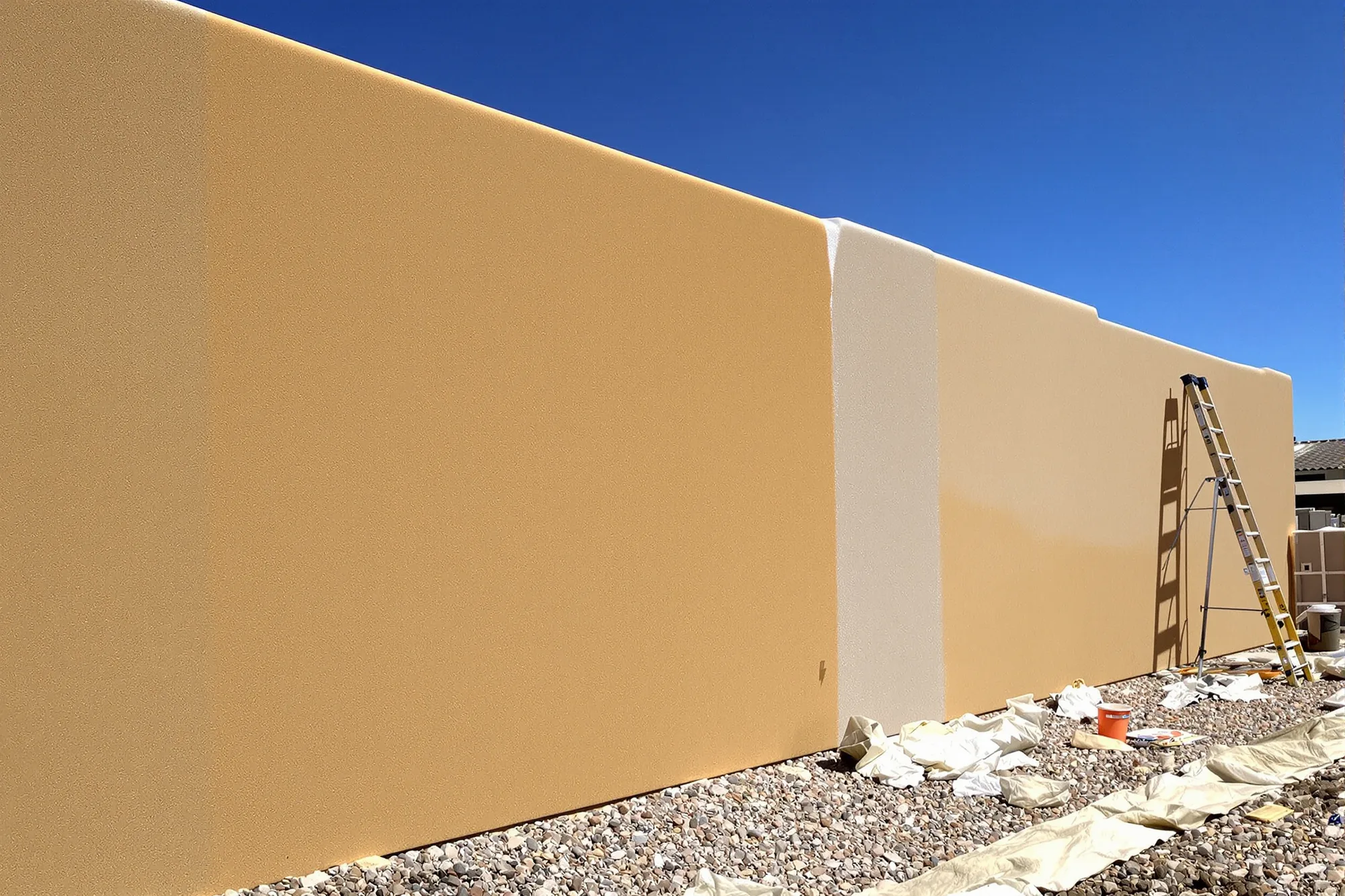 Tan stucco ranch home wall half repainted in a rich sand color beside the faded original